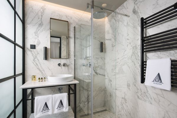 Luminous charm of the Deluxe Mezzanine Double Room's bathroom at Almayer Art & Heritage Hotel, featuring bright marble tiles and a refreshing walk-in rain shower