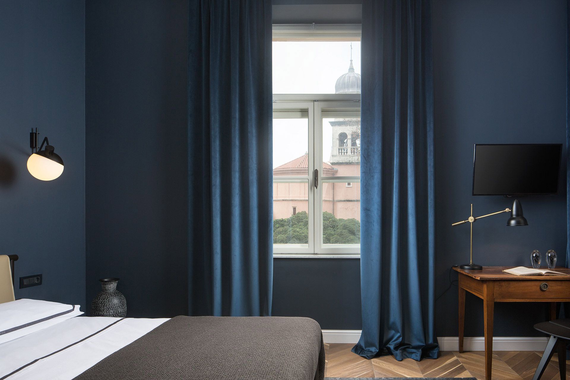 Comfy queen-size bed and bright windows in Almayer hotel’s deluxe double room Bianchini in dependance